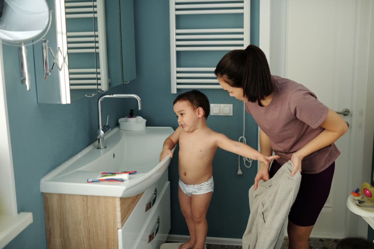 A mother helps her young son wash his hands at the bathroom sink